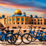An image that showcases a colorful array of electric bikes lined up neatly against a backdrop of Jerusalem's iconic landmarks, enticing readers to discover the affordable rental rates for these eco-friendly vehicles