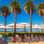 An image showcasing a vibrant beachside scene in Santa Monica, with a row of colorful electric bikes lined up on a sunny, palm tree-lined street, ready for rent